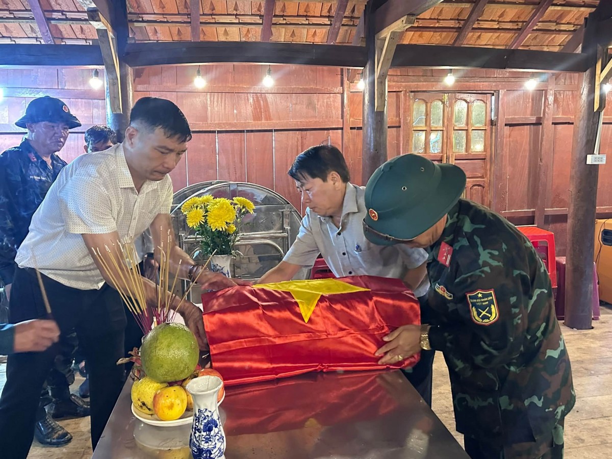 Cán bộ, chiến sĩ và chính quyền địa phương thực hiện nghi thức phủ Quân kỳ, chuẩn bị đưa hài cốt liệt sĩ tìm thấy tại thôn Tu Thó (xã Măng Ri) về nơi an nghỉ.